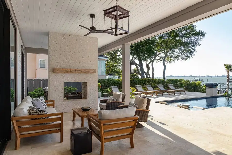 Covered outdoor room with fireplace overlooking the pool and water